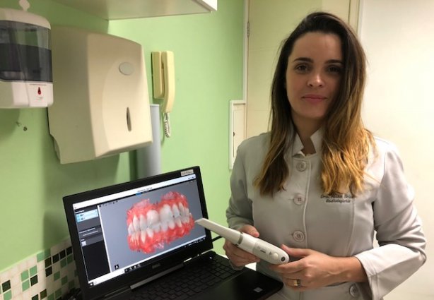 Aline Brum segura o aparelho de escaneamento intra oral colorido, a última inovação da clínica Faces Diagnósticos